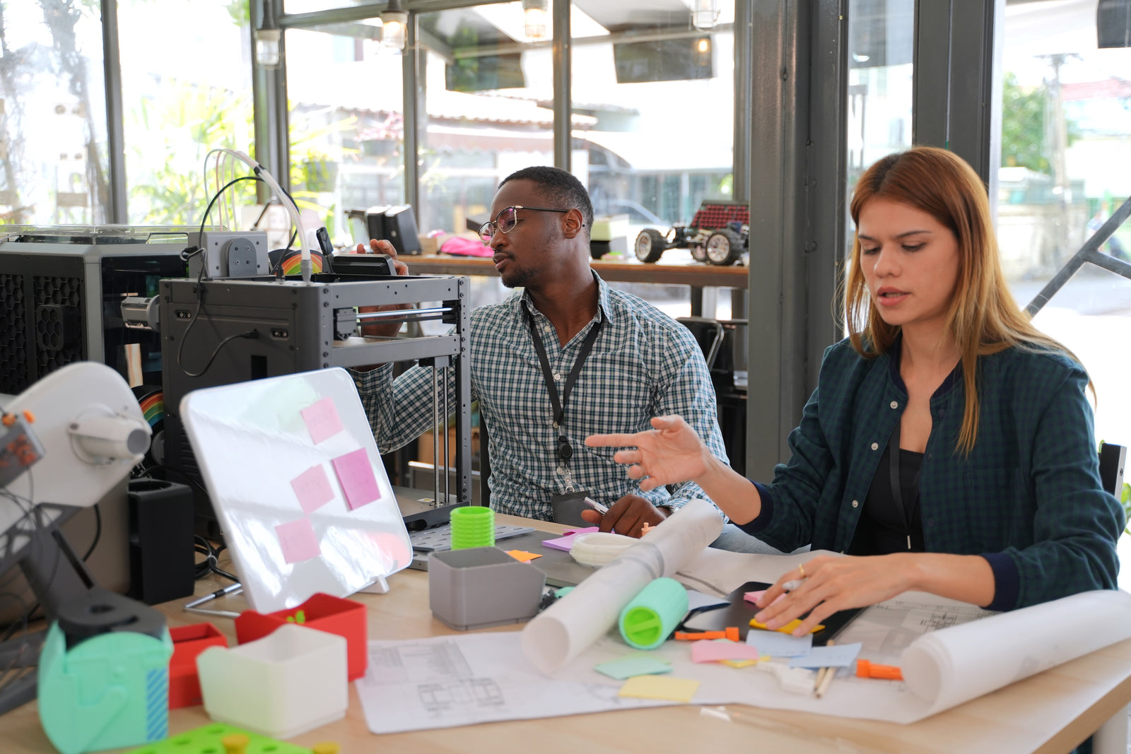 Two people collaborating on a 3D printing project with a desktop 3D printer and printed components