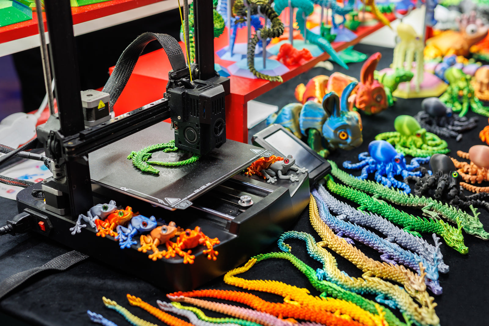 A desktop 3D printer printing a green and yellow object, surrounded by colorful printed figures.